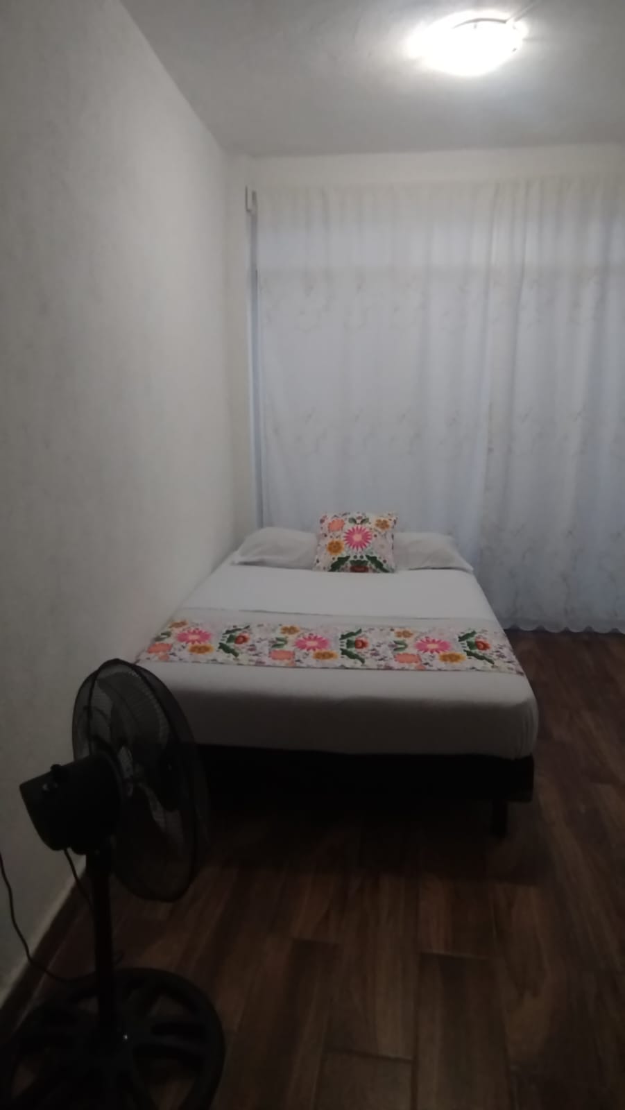 Fotografía de habitación con cama y ventilador de piso.